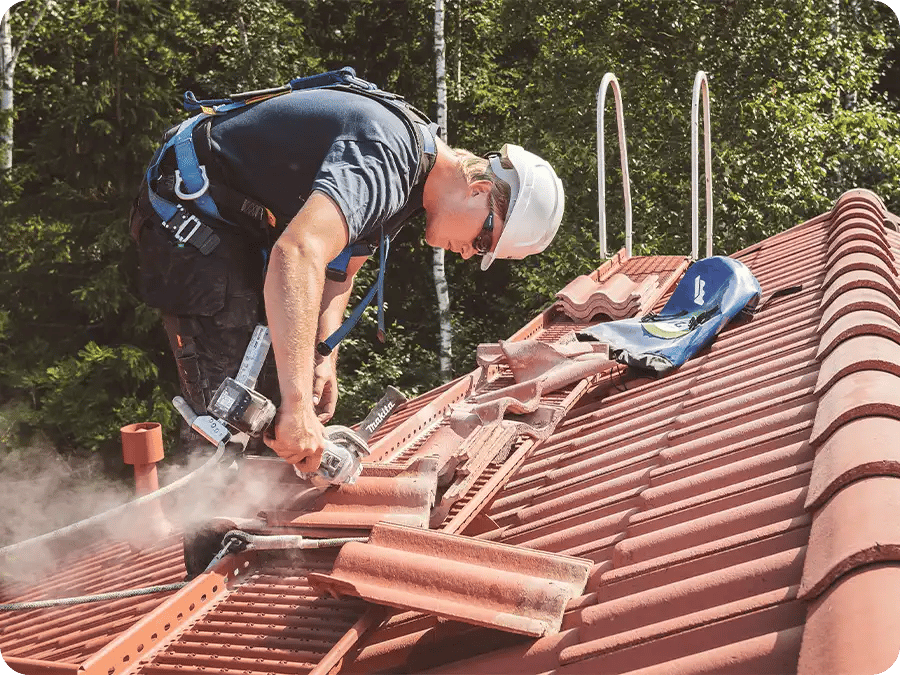 Mies tekemässä tiilikaton huoltoa vaihtaen rikkinäisiä kattotiiliä uusiin.